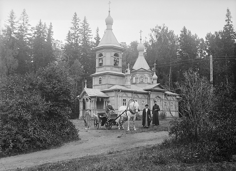Люди и конный экипаж возле деревянной церкви.