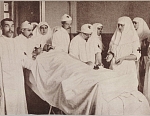 Княжна Вера Гедройц проводит операцию. Ассистирует Императрица Александра Федоровна с Великими Княжнами. В изголовье стоит А. А. Вырубова.